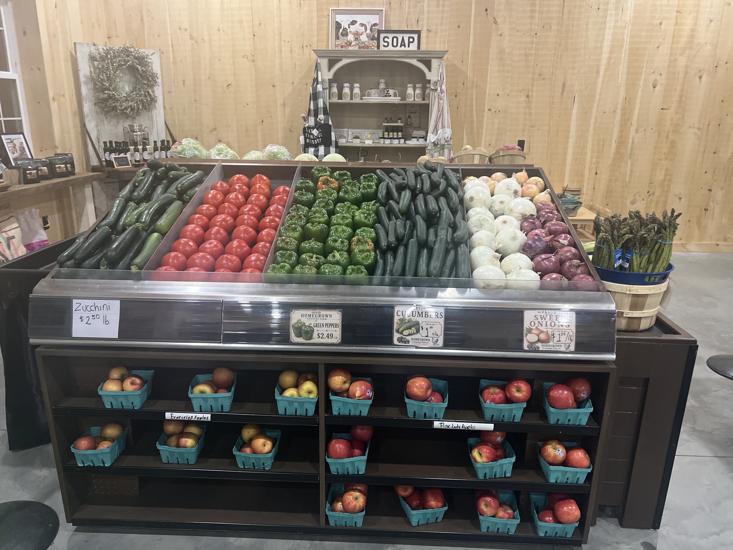 Country store produce bins with zucchini, tomatoes, peppers, cucumbers, onions, and apples