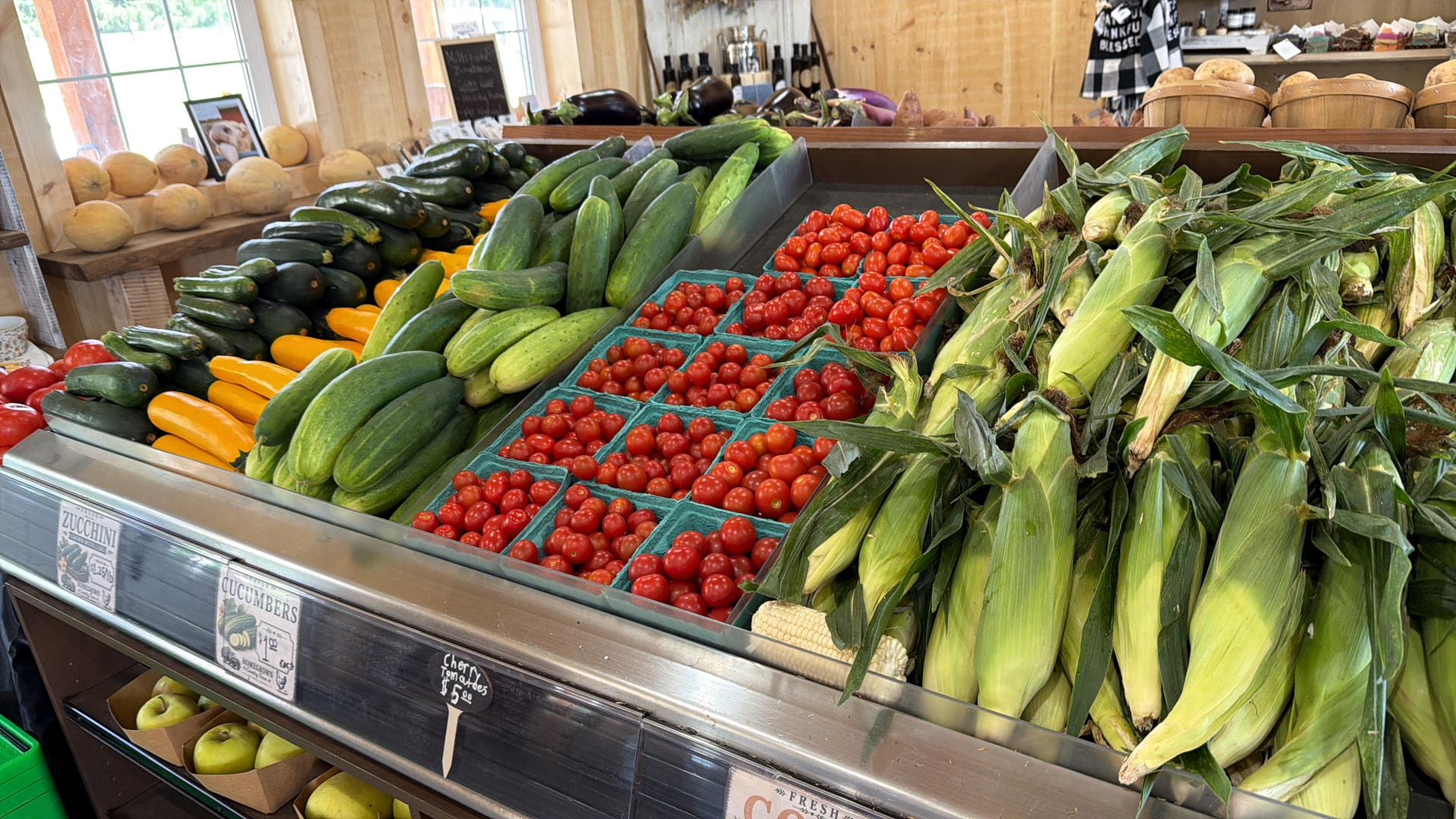 Farmstand produce tables with sweet corn, cucumbers, zucchini and cherry tomatoes
