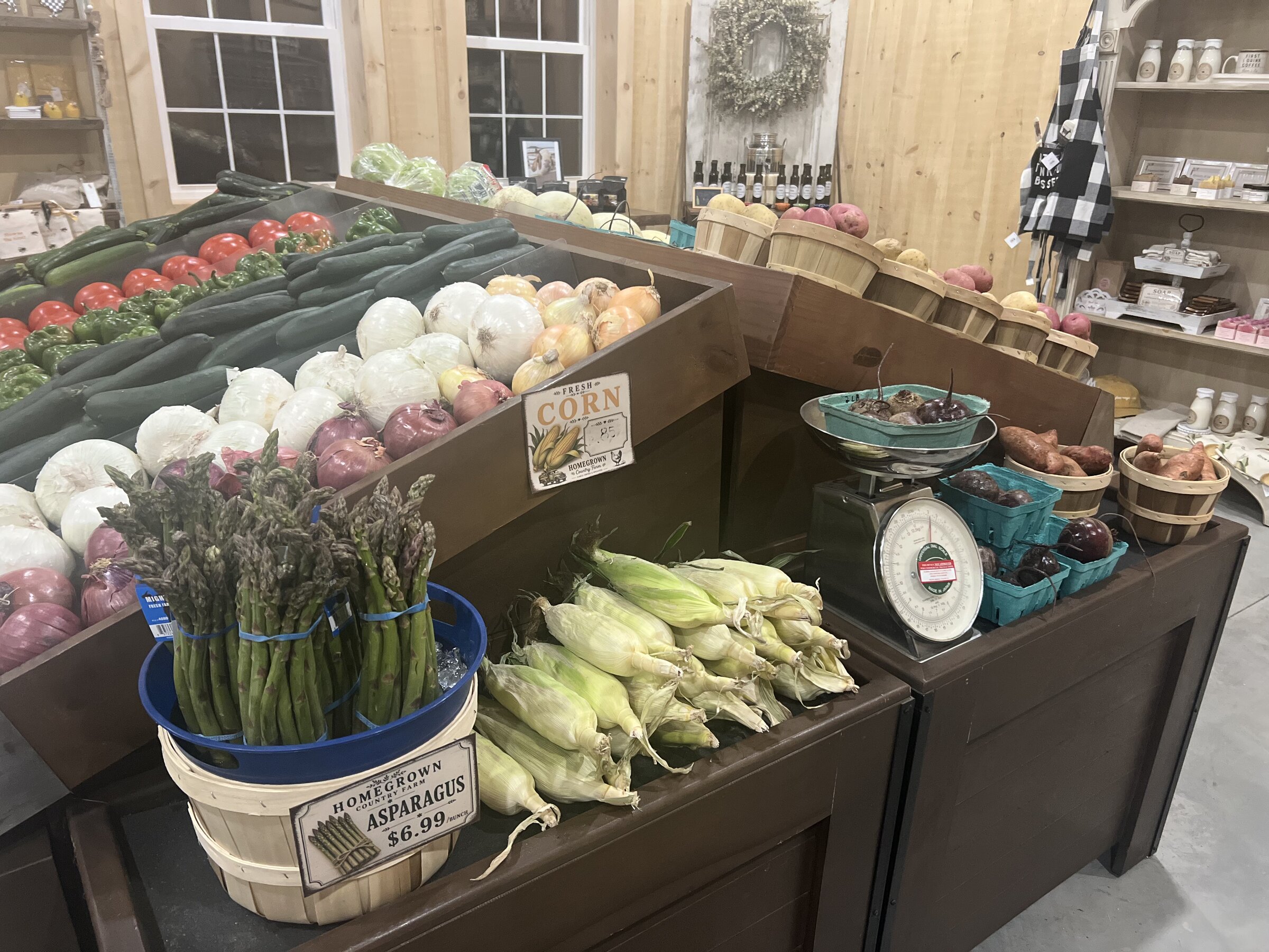 Country store produce tables with onions, asparagus, corn, and root vegetables